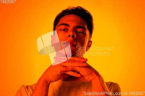 Image of Handsome caucasian man\'s portrait isolated on orange studio background in neon light, monochrome