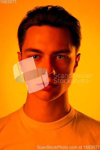 Image of Handsome caucasian man\'s portrait isolated on orange studio background in neon light, monochrome