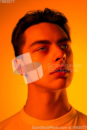 Image of Handsome caucasian man\'s portrait isolated on orange studio background in neon light, monochrome