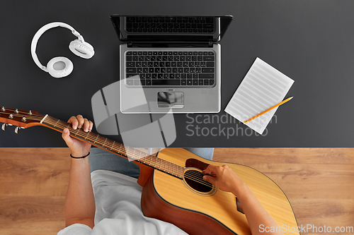 Image of young man with laptop playing guitar at table