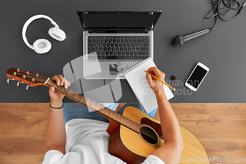 Image of man with guitar writing to music book at table