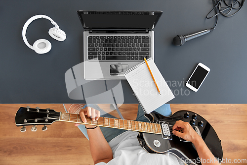 Image of young man with laptop playing guitar at table