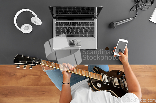 Image of young man with guitar and smartphone at table