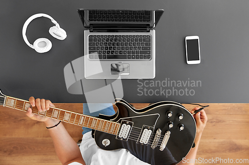 Image of young man with laptop tuning guitar at table