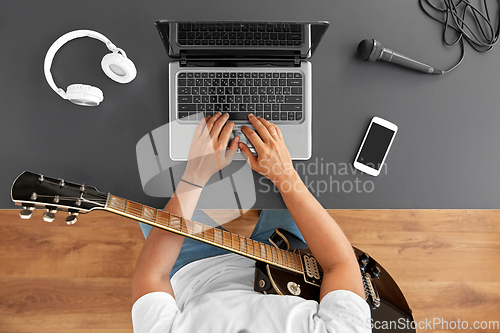 Image of young man with laptop and guitar at table