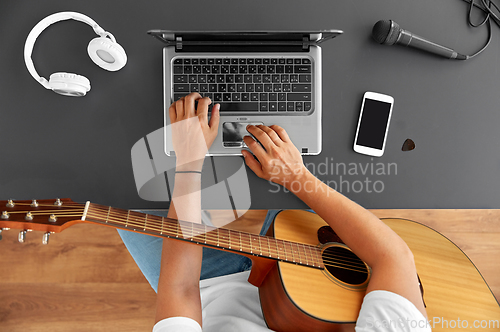 Image of young man with laptop playing guitar at table