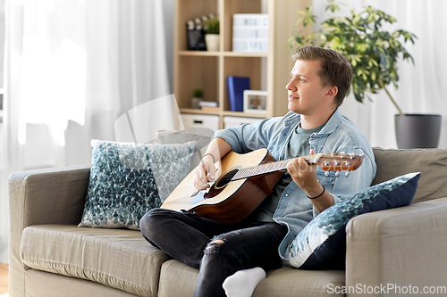 Image of young man playing guitar sitting on sofa at home