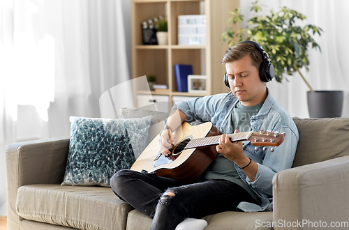 Image of man in headphones playing guitar at home