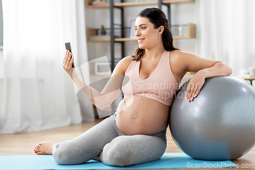 Image of pregnant woman with phone and fitness ball at home