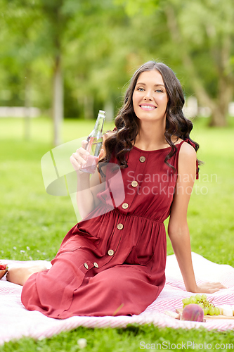 Image of happy woman with drink in bottle at picnic in park