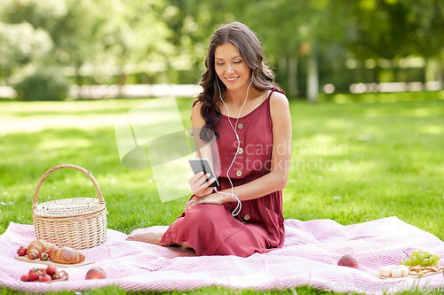 Image of woman with smartphone and earphones at picnic