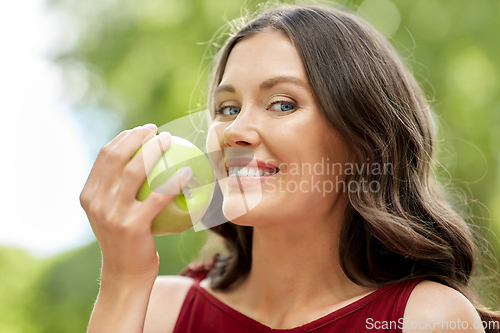Image of happy woman eating green apple at summer park