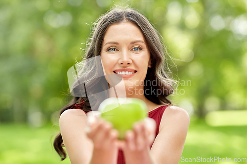 Image of happy woman eating green apple at summer park