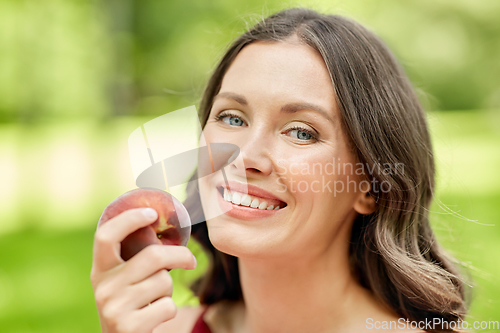 Image of happy woman eating peach at summer park