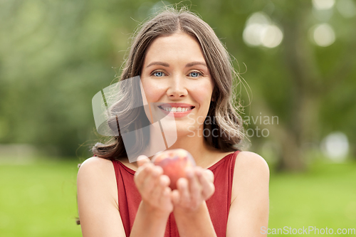 Image of happy woman eating peach at summer park