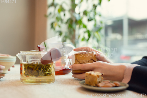 Image of Close up female hands pouring tea in cup at restaurant or cafe, daily lifestyle