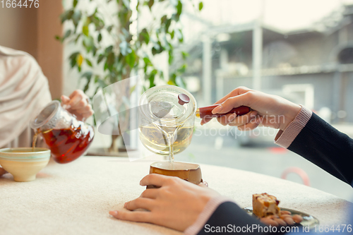 Image of Close up female hands pouring tea in cup at restaurant or cafe, daily lifestyle