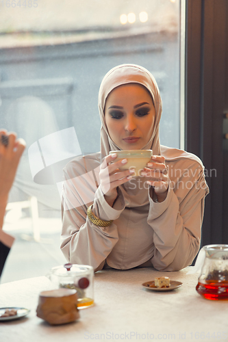 Image of Beautiful arab woman meeting at cafe or restaurant with friend, spending time with cup of tea