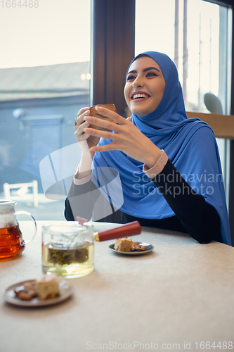 Image of Beautiful arab woman meeting at cafe or restaurant with friend, spending time with cup of tea