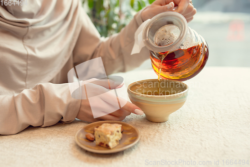 Image of Close up female hands pouring tea in cup at restaurant or cafe, daily lifestyle