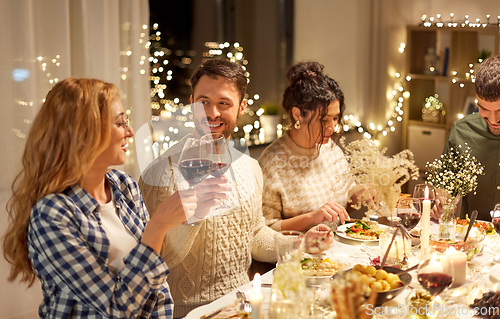 Image of happy friends drinking red wine at christmas party