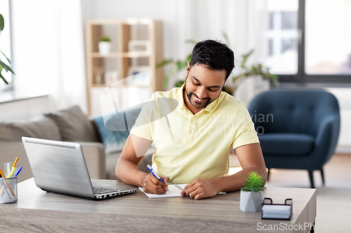 Image of indian man with notebook and laptop at home office