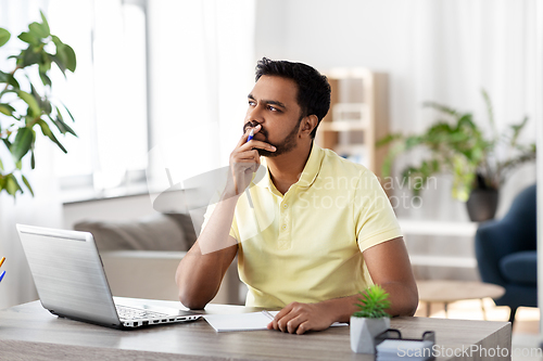 Image of indian man with notebook and laptop at home office