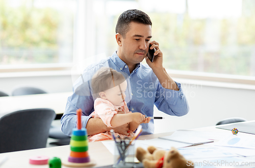 Image of father with baby calling on phone at home office