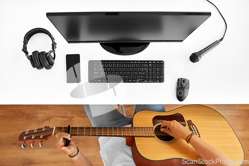 Image of young man with computer playing guitar at table