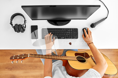 Image of young man with computer and guitar at table