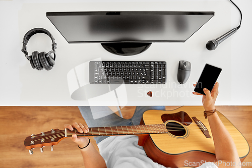 Image of young man with guitar and smartphone at table