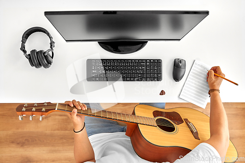 Image of man with guitar writing to music book at table