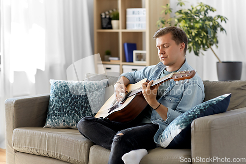 Image of young man playing guitar sitting on sofa at home