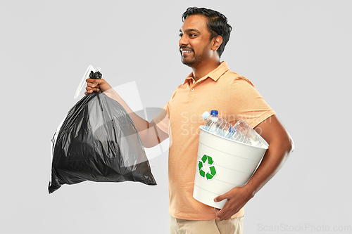 Image of smiling indian man sorting paper and plastic waste