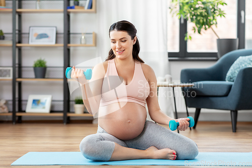 Image of pregnant woman with dumbbells doing sports at home