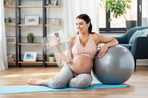 Image of pregnant woman with phone and fitness ball at home