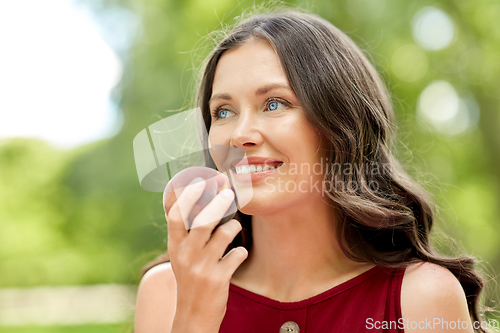 Image of happy woman eating peach at summer park