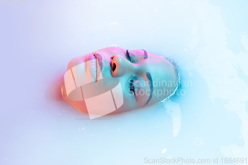 Image of Close up female face in the milk bath with soft glowing in neon light