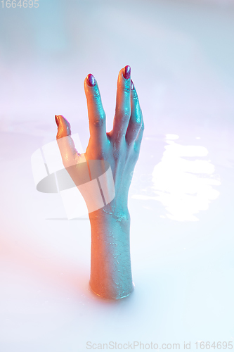 Image of Close up female hand gesturing from the milk bath with soft glowing in neon light