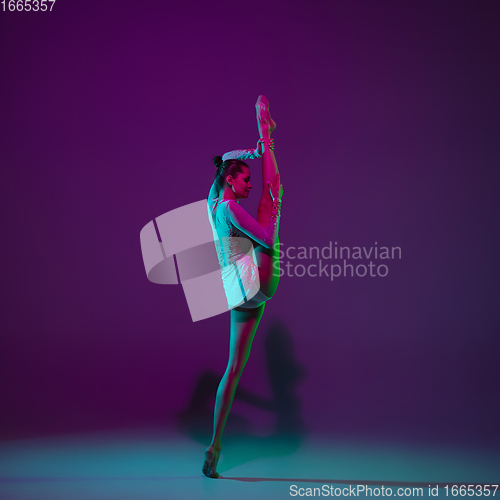 Image of Young female athlete, rhythmic gymnastics artist on purple background with neon light. Beautiful girl practicing with equipment. Grace in performance.