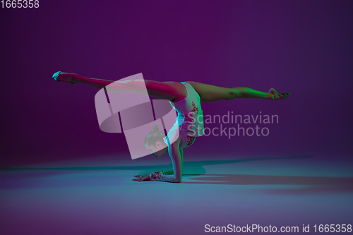 Image of Young female athlete, rhythmic gymnastics artist on purple background with neon light. Beautiful girl practicing with equipment. Grace in performance.