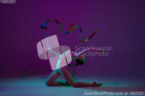 Image of Young female athlete, rhythmic gymnastics artist on purple background with neon light. Beautiful girl practicing with equipment. Grace in performance.