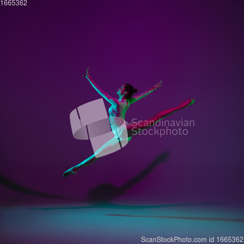 Image of Young female athlete, rhythmic gymnastics artist on purple background with neon light. Beautiful girl practicing with equipment. Grace in performance.