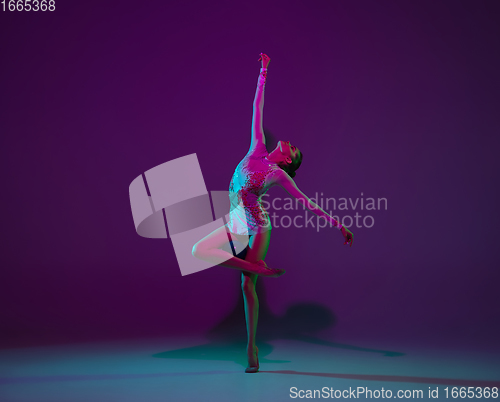 Image of Young female athlete, rhythmic gymnastics artist on purple background with neon light. Beautiful girl practicing with equipment. Grace in performance.