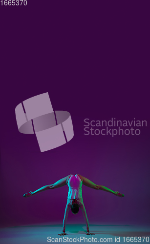 Image of Young female athlete, rhythmic gymnastics artist on purple background with neon light. Beautiful girl practicing with equipment. Grace in performance.