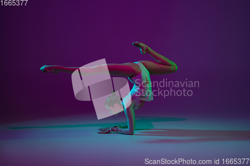 Image of Young female athlete, rhythmic gymnastics artist on purple background with neon light. Beautiful girl practicing with equipment. Grace in performance.