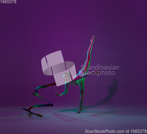 Image of Young female athlete, rhythmic gymnastics artist on purple background with neon light. Beautiful girl practicing with equipment. Grace in performance.