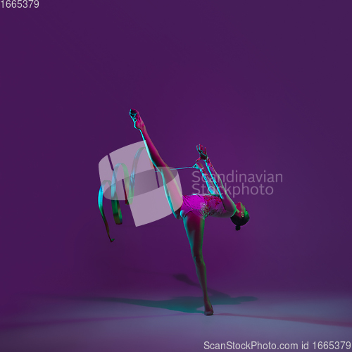 Image of Young female athlete, rhythmic gymnastics artist on purple background with neon light. Beautiful girl practicing with equipment. Grace in performance.