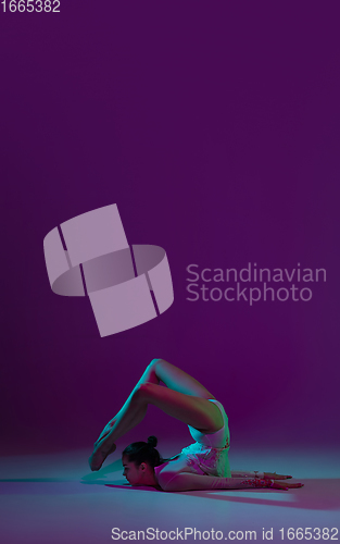 Image of Young female athlete, rhythmic gymnastics artist on purple background with neon light. Beautiful girl practicing with equipment. Grace in performance.