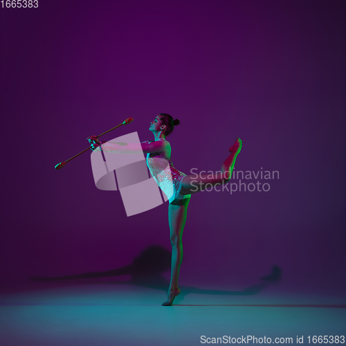 Image of Young female athlete, rhythmic gymnastics artist on purple background with neon light. Beautiful girl practicing with equipment. Grace in performance.